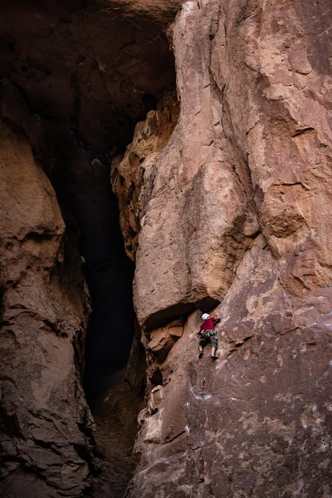 A climber in Gualjaina, Chubut, navigates a steep rocky cliff face under natural light.