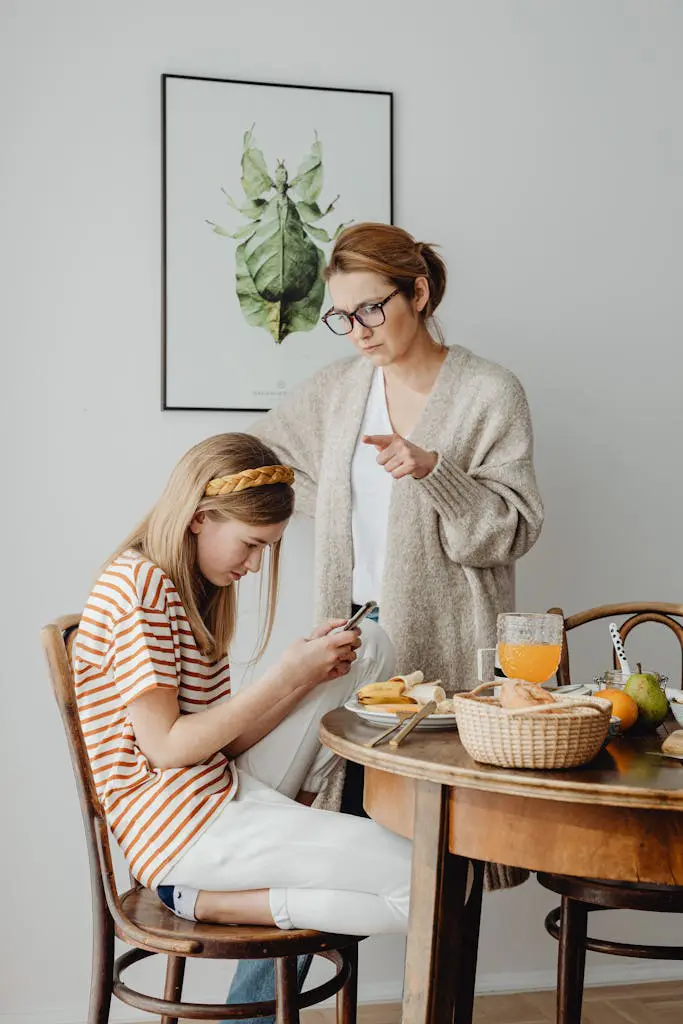 A mother and daughter in a serious conversation at the dining table with a smartphone in focus.