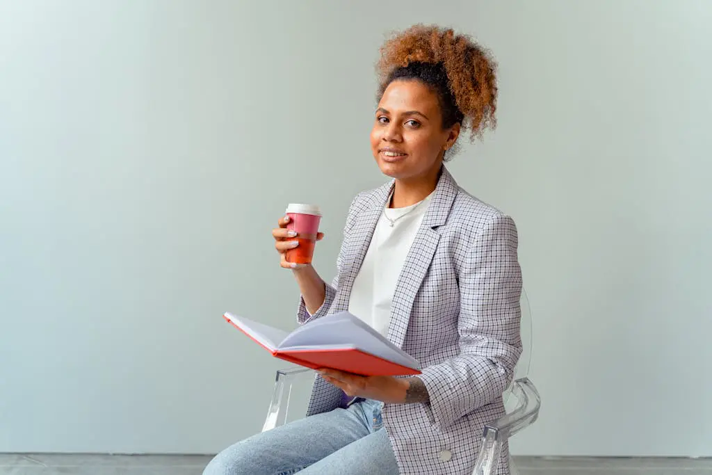 Smiling professional woman holding a coffee and notebook in a light office setting, exuding confidence and knowledge.